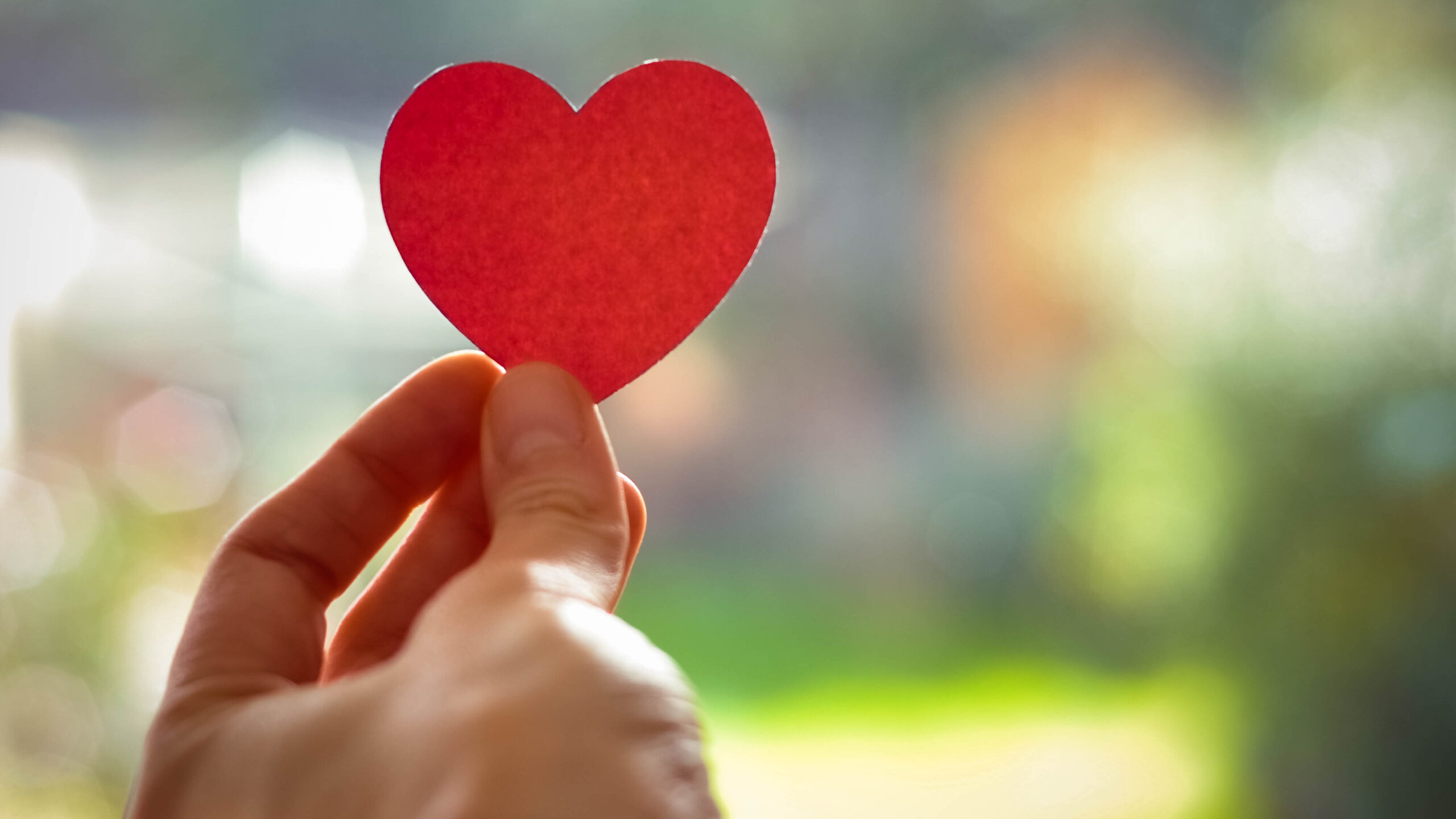 Person's hand holding a red paper heart-shaped cutout.