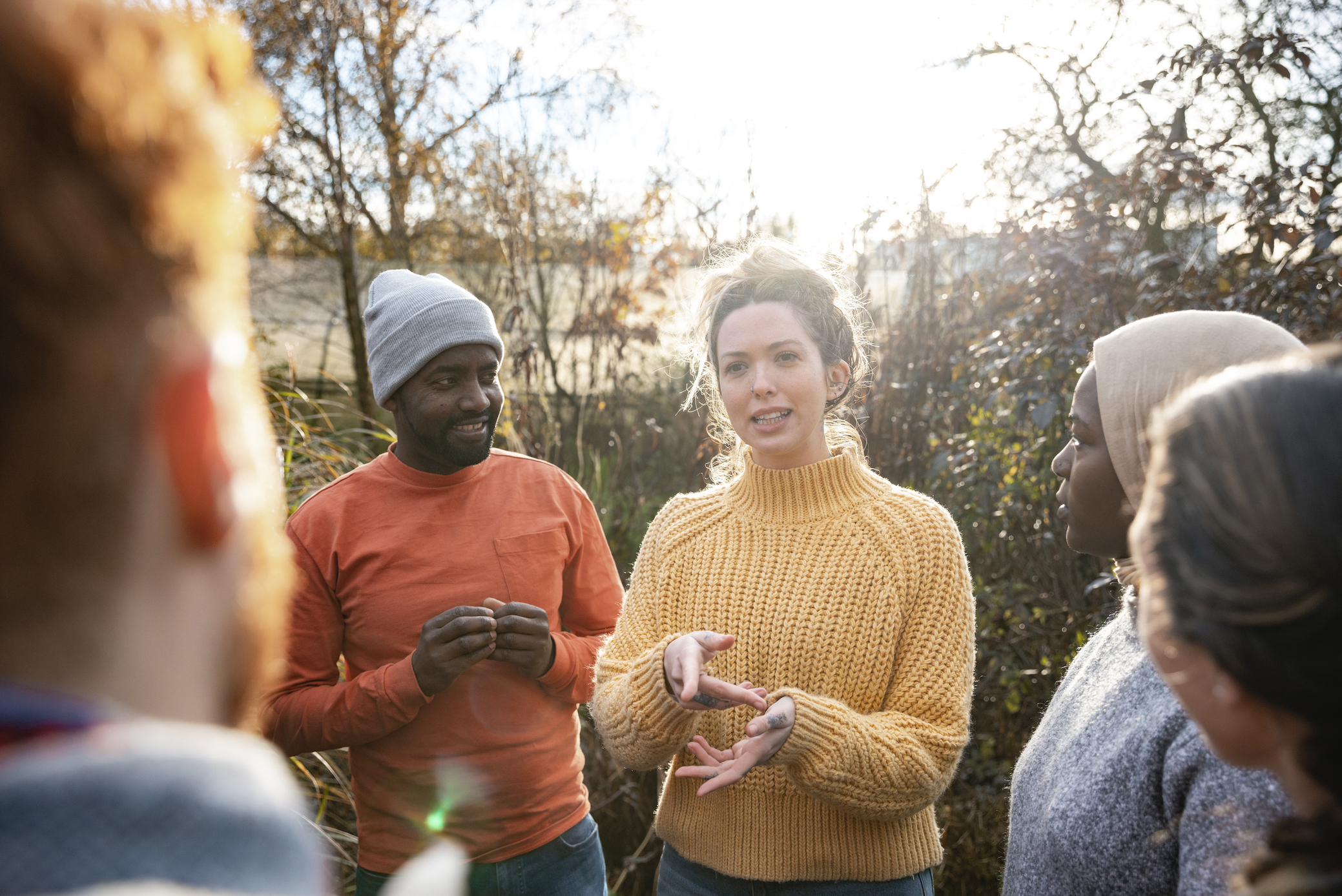 Young woman leads a group of five men and women of various ages in discussion outdoors.